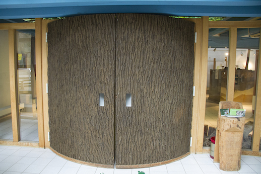 Eine große, halbrunde Tür in Form eines Baumstammes ist der EIngang in die Ausstellung.