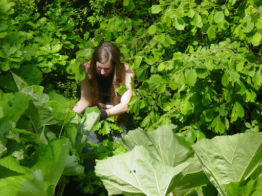 Eine junge Frau geht untersuchend durch einen von Wasserpflanzen dicht bewachsenen Bach.